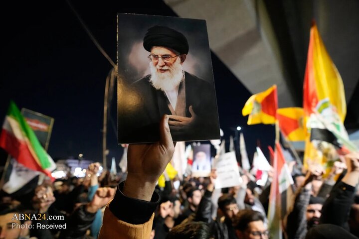 معترضی با در دست داشتن تصویر آیت‌الله علی خامنه‌ای در جریان تجمع اعتراضی علیه حملات آمریکا و اسرائیل به ایران، بر روی پل منتهی به منطقه سبز Green Zone در بغداد.